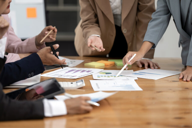 Group of confident business people point to graphs and charts to analyze market data and balance sheet, sitting at desk office.