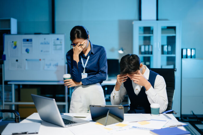 Asian business colleagues feeling stress and exhaustion from workload, overworked team facing deadline pressure and burnout in modern office at night.